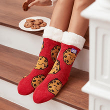 Load image into Gallery viewer, The Foozie™ Cookie Red slipper socks, worn sitting on a wooden stair beside a plate of cookies